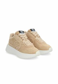 Beige suede sneakers with a textured white sole, rounded shape, lace closure, and plush lining. Features a black logo tag on the tongue.