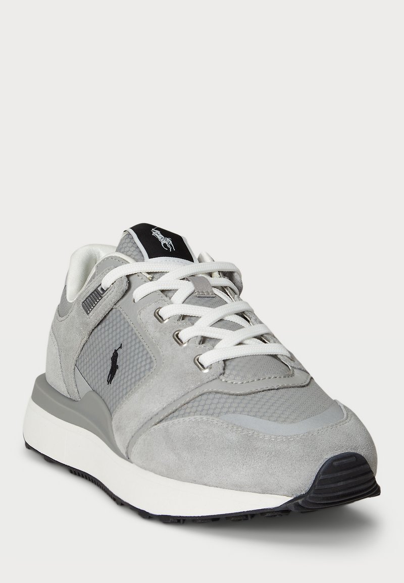 Grauer Wildleder- und Mesh-Sneaker mit weißen Schnürsenkeln, einem schwarzen Logo auf der Zunge und einer strukturierten Sohle. Merkmale sind eine abgerundete Zehenpartie und ein gepolsterter Schaft.