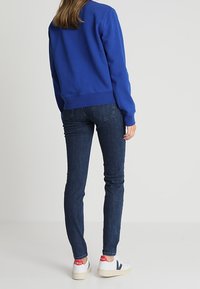 Modrá mikina s žebrovanými lemy a manžetami, spárovaná s tmavě modrými skinny džíny a bílými teniskami s červenými a námořnickými akcenty.