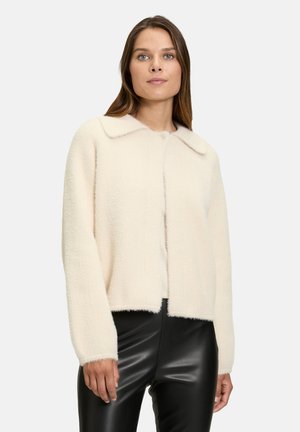 Crème-kleurige cropped trui met een zachte, gestructureerde afwerking, voorzien van een grote kraag en een sluiting aan de voorkant, gecombineerd met zwarte nep-lederen broek.