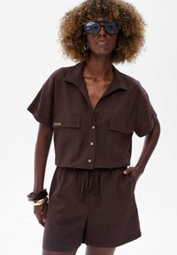 Bruine linnen twee-delig set met korte mouwen, een knoopsluiting aan de bovenkant en shorts met een elastische taille. Voorzien van twee voorkzaken en een trekkoord.