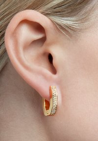 Orecchino a cerchio in oro con superficie texture, caratterizzato da una fila di piccole pietre scintillanti lungo un lato, indossato in un orecchio.