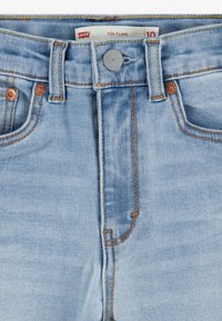 Ljusblå denimjeans, högmidjade med utsvängd stil, med kopparknappar, orange sömnad och klassisk femfickdesign.