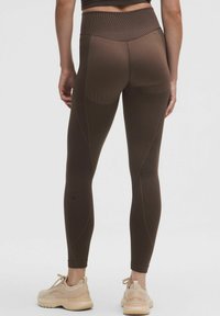 Leggings marron taille haute avec texture côtelée, silhouette ajustée et coutures courbées. Associés à des chaussures de sport beige clair.