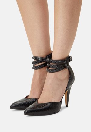 Czarne szpilki z teksturą krokodyla i spiczastym noskiem, z wieloma paskami wokół kostki, ozdobione metalowymi ćwiekami i klamrami.