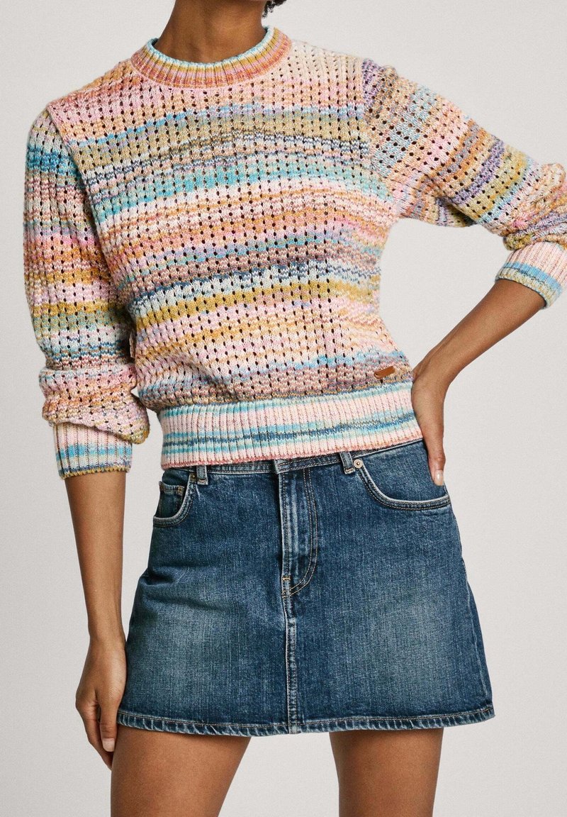 Femme portant un pull en maille rayé multicolore avec des manches bouffantes et une mini-jupe en jean bleu taille haute.