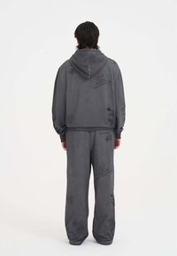 Szara bluza i spodnie z miękkiego materiału, z grafikom i tekstem na całej powierzchni. Bluza ma sznurki i kieszeń kangurkę.