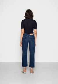 Modré džíny s vysokým pasem a rovnými nohavicemi, se dvěma zadními kapsami a béžovou nášivkou na pase, spárované s přiléhavým černým topem.