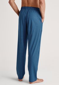 Blauwe gemusterde pyjamabroek met een losse pasvorm, elastische tailleband, zijzakken en een klein herhalend stippenpatroon op een gladde stof.