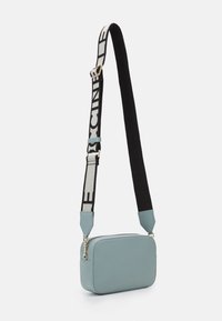 Prostokątna torebka na ramię ze światłoniebieskiej skóry o teksturowanym wykończeniu, wyposażona w czarno-biały regulowany pasek i złote detale.