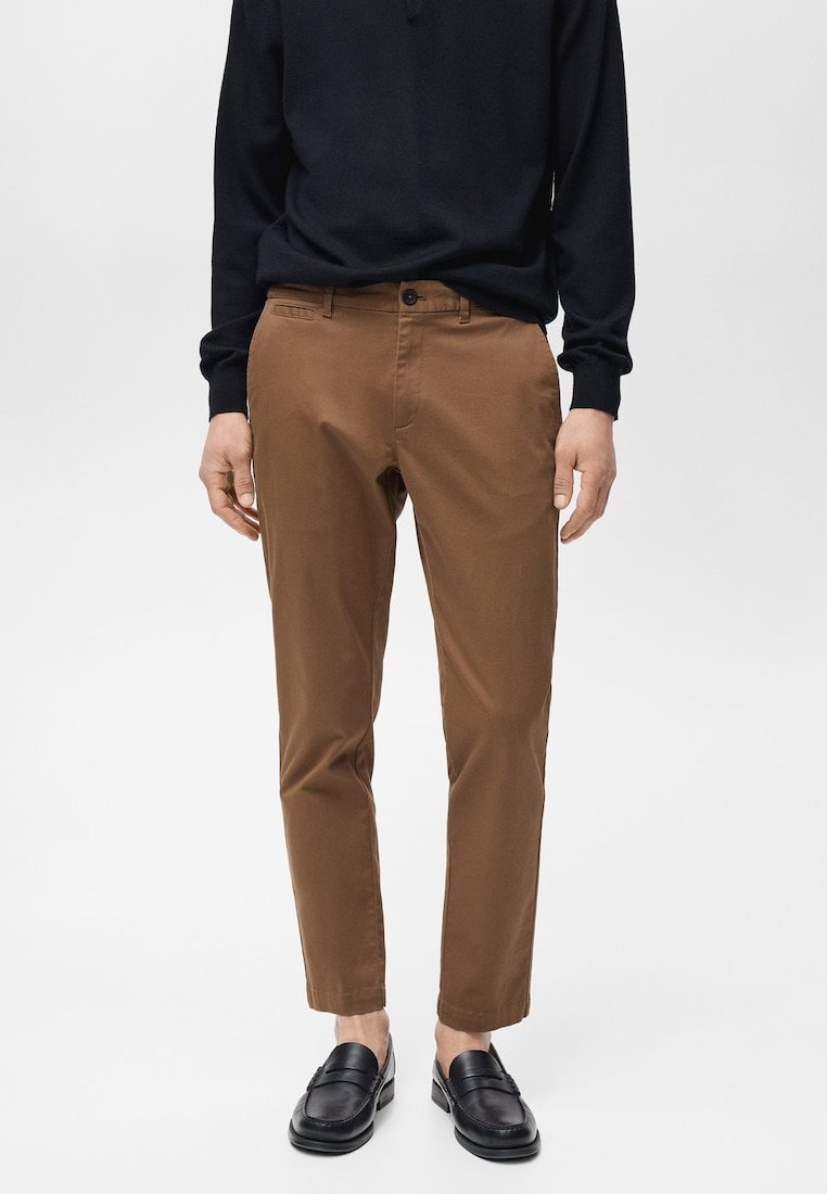 Hnedé bavlnené nohavice so slim fit strihom, predné vrecká a zapínanie na gombík, v kombinácii s čiernou košeľou s dlhým rukávom a čiernymi mokasínami.