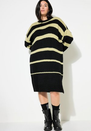Zwarte en limoen gestreepte oversized gebreide sweaterdress met geribde manchetten en zoom, gecombineerd met zwarte enkellaarsjes en patroonkousen.