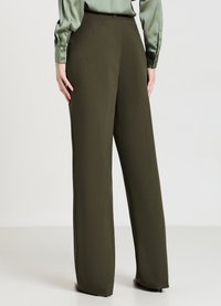 Olivgrüne weit geschnittene Hosen aus einem glatten Stoff, mit einem taillierten Bund und klaren Linien. Kombiniert mit einer hellgrünen Bluse.