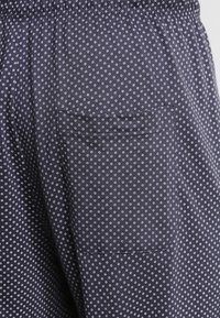 Navyfarbene Stoffshorts mit einem weißen Punktenmuster, elastischem Bund und einer aufgesetzten Tasche an der Seite. Weicher Stoff, lässiges Design.