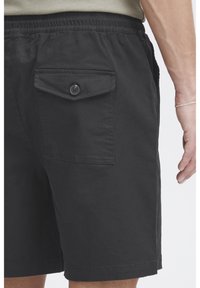 Mustad lühikesed püksid, millel on elastne vöökoht, üks nööbitav tagatasku ja sile tekstuur sirge äärega.