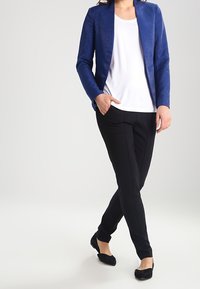 Marinblå skräddarsydd kavaj med en slät textur, bärs över en vit t-shirt. Svarta slim-fit byxor och svarta platta skor fulländar outfiten.