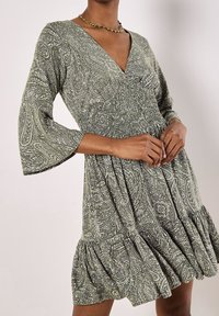 Green paisley dress with a V-neck, three-quarter bell sleeves, gathered bodice, and a ruffled hem. Fabric has a textured, patterned design.