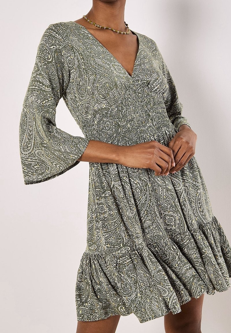 Green paisley dress with a V-neck, three-quarter bell sleeves, gathered bodice, and a ruffled hem. Fabric has a textured, patterned design.