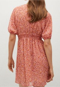 Robe fleurie rose avec des manches courtes bouffantes, taille froncée et tissu léger, présentant un petit motif floral sur l'ensemble.