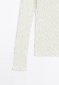 Langsleeve top in off-white, textuurstof met een subtiel zigzagpatroon. De randen zijn ongelijk gesneden, wat een zachte afwerking creëert.