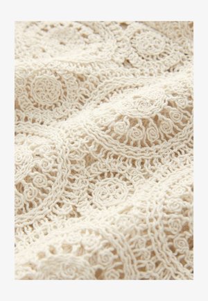 Crocheted fabric in off-white with intricate circular and floral patterns, featuring a textured finish and delicate, open weave.