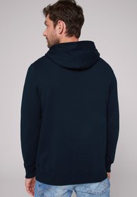 Granatowa bluza z kapturem o strukturalnej fakturze, z prążkowanymi mankietami i dołem. Prosty design, bez widocznych wzorów czy logo.