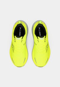Ein Paar leuchtend gelbe Laufschuhe mit grauen Sohlen und schwarzem Innenfutter, von oben auf einem weißen Hintergrund betrachtet.