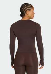 Bruine lange mouwen sporttop met een aansluitend ontwerp, gemaakt van een glad, rekbaar materiaal, voorzien van een ronde halslijn en duimgaten.