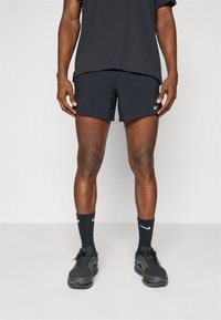 Schwarze Sportshorts aus strukturiertem Stoff mit einem kleinen weißen Nike-Logo. Kombiniert mit schwarzen Schuhen und Socken, alles in neutralen Farben.