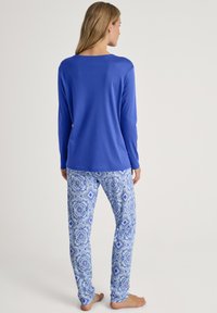 Langärmliges blaues Oberteil kombiniert mit gemusterten hellblauen Schlafanzughosen, die florale und geometrische Designs aufweisen, von hinten präsentiert.