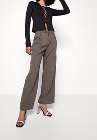 Maglietta nera a maniche lunghe con scollatura allacciata, abbinata a pantaloni taupe a vita alta e morbidi, e sandali con tacco argentati.