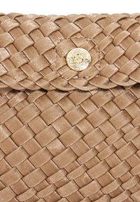 Close-up van een tan geweven leren tasflap met een ronde gouden knop met gegraveerde merkinitialen.
