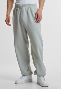 Helle graue Sweatpants aus einem weichen, dehnbaren Stoff mit einem elastischen Bund, in entspannter Passform und mit seitlichen Taschen. Tragen Sie sie mit weißen Sneakers.