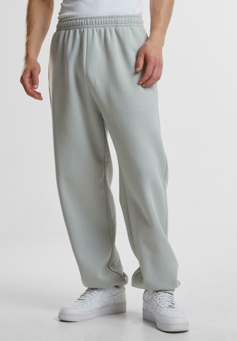 Helle graue Sweatpants aus einem weichen, dehnbaren Stoff mit einem elastischen Bund, in entspannter Passform und mit seitlichen Taschen. Tragen Sie sie mit weißen Sneakers.