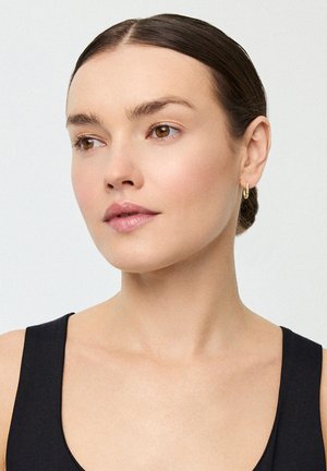 Złota kolczyk w kształcie obręczy, gładka skóra, brązowe oczy, lekki makijaż. Ciemna bezrękawnikowa bluzka z kołnierzykiem. Neutralne tło. Czysty i prosty design.