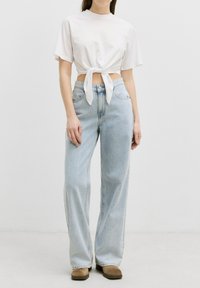 Witte cropped t-shirt met een knoop aan de voorkant, gecombineerd met hooglopende lichtblauwe wijde jeans en bruine enkellaarsjes. Eenvoudige, casual look.