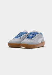 Zapatillas de ante gris con cordones azules con estampado, logotipo blanco en el lateral y suela de goma marrón; diseño de punta redondeada y cuello acolchado.