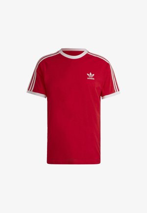 T-shirt rouge Adidas avec col rond blanc, bords de manches blancs, trois bandes sur les épaules et logo trèfle Adidas sur la poitrine.