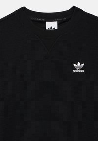 Μαύρο φούτερ με υφή βελόνας βάφλας και στρογγυλή λαιμόκοψη, με λευκό λογότυπο Adidas στο αριστερό στήθος και υφασμάτινη υφή.