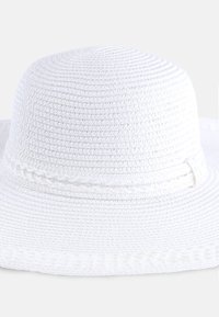 Biały, pleciony kapelusz przeciwsłoneczny z zaokrągloną koroną i szerokim rondem, ozdobiony plecioną taśmą wokół podstawy, która dodaje szczegółu i tekstury.