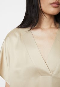 Haut en satin beige avec un décolleté en V profond, manches kimono courtes et détails de couture soignés, présentant une texture lisse et brillante.