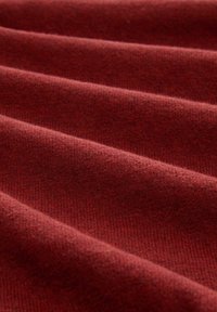 Roter Wollstoff mit gerippter Textur, der weiche Falten und Tiefe aufweist. Die Oberfläche hat einen subtilen Glanz und eine warme, reichhaltige Farbe.