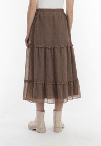 Gonna midi a strati marrone realizzata in un tessuto leggero e strutturato con un motivo floreale. La vita elasticizzata e i dettagli a volant arricchiscono il design.