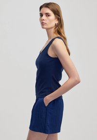 Marineblauwe tanktop met brede banden en een ronde halslijn, gecombineerd met gestructureerde marineblauwe shorts met zijvakjes. Glad stoftextuur.