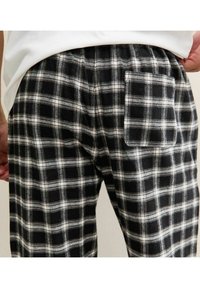 Black and white plaid pajama pants made of soft fabric, featuring an elastic waistband and a back pocket. The pattern consists of alternating squares.