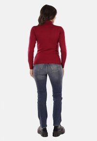 Maglione a collo alto bordeaux aderente abbinato a jeans blu scuro. I jeans presentano tasche posteriori e un design slim, completati da stivali neri.