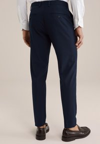 Tumši zili šūti bikses ar šauru piegriezumu, ar aizmugurējām kabatām un pogu akcentiem, apvienotas ar tumši brūnām kurpēm.