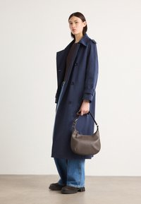 Námořnický modrý trench coat s velkými knoflíky, límcem a detaily na manžetách. Ve spojení s džíny a hnědou koženou kabelkou přes rameno.