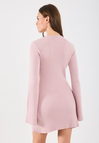 Žíhané pletené šaty v bledoružovej farbe s dlhými roztvorenými rukávmi a priliehavým strihom, s okrúhlym výstrihom a rozparokmi po stranách.