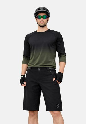 Mann trägt langärmliges Fahrradtrikot in Schwarz und Grün, schwarze Shorts, schwarze fingerlose Handschuhe, grüne reflektierende Sonnenbrille und schwarzen Fahrradhelm.